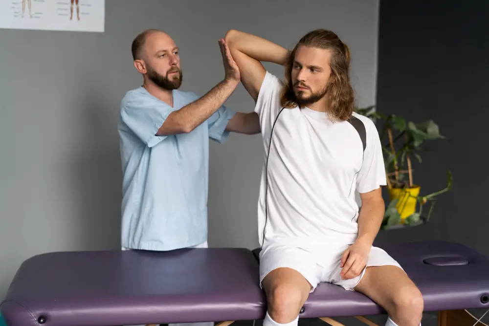 A therapist helps a man perform a shoulder stretch on a treatment table.