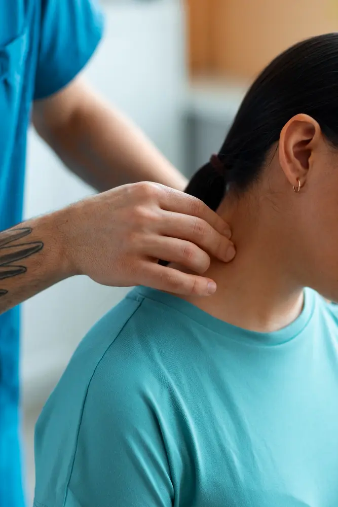 A healthcare professional gently examines or massages the side of a woman’s neck while she sits upright, suggesting assessment or treatment for neck pain in a clinical setting.