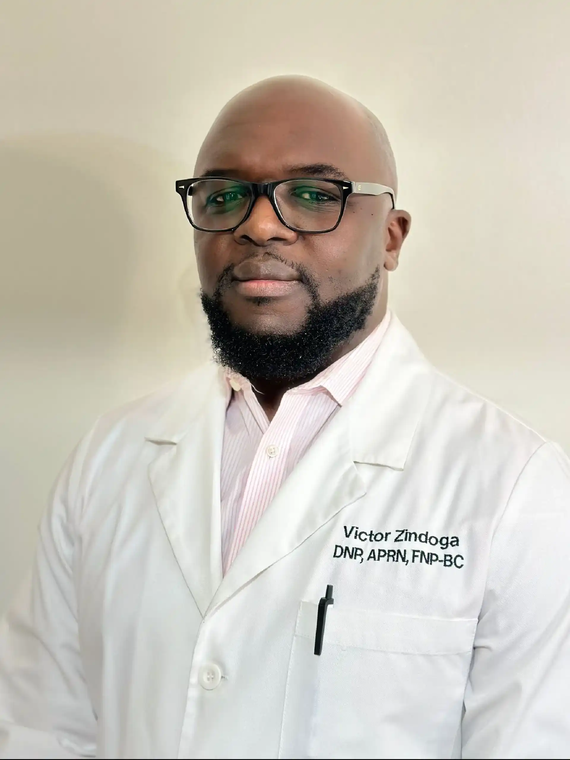 Person wearing glasses and a white lab coat with embroidered name and credentials, standing against a light background.