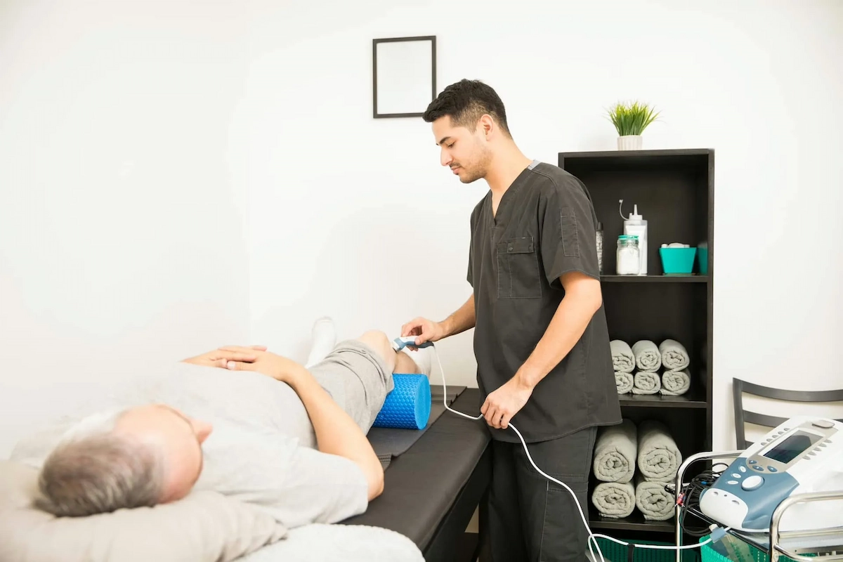 Chiropractic assistant helping a patient with knee pain with shockwave therapy