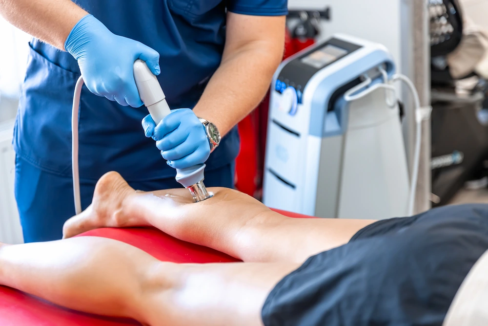 Physiotherapist performing shockwave therapy on a patient's lower leg for pain relief.